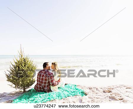 Stock Photo - Loving couple sitting on beach with tree. Fotosearch