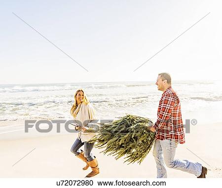 Stock Image - Loving couple walking on beach with tree. Fotosearch