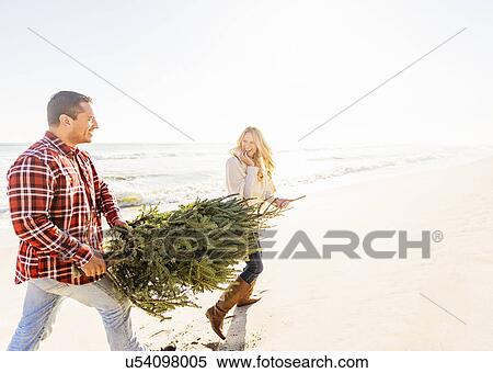 Stock Photography - Loving couple walking on beach with tree. Fotosearch