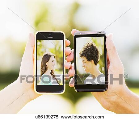 Stock Photography - Man and teenage girl (14-15) holding smart phones with photos of themselves. Fotosearch
