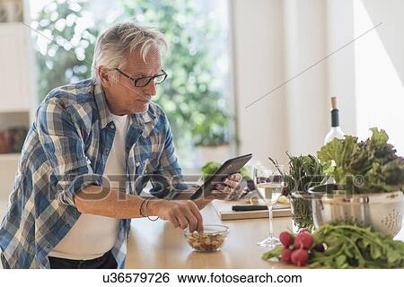 Man in kitchen using tablet View Large Photo Image Stock Photograph - Man in kitchen using tablet. Fotosearch