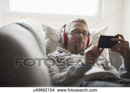Picture - Man lying on sofa listening to music. Fotosearch