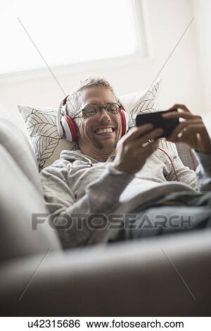 Stock Photograph - Man lying on sofa listening to music. Fotosearch