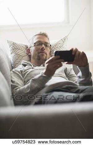 Man lying on sofa using phone View Large Photo Image Stock Image - Man lying on sofa using phone. Fotosearch