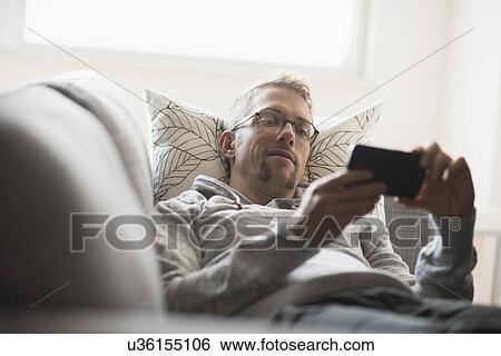 Stock Photograph - Man lying on sofa using phone. Fotosearch