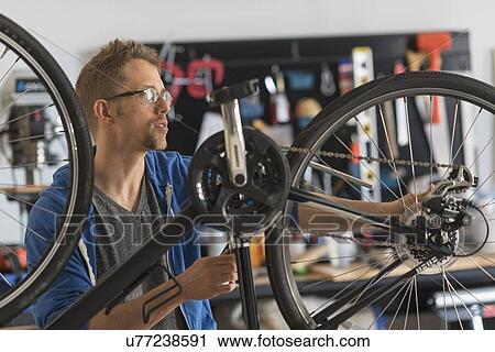 Stock Image - Man repairing bike in shop. Fotosearch