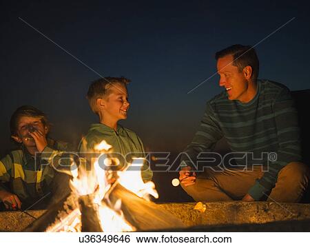 Stock Photograph - Man talking with his sons (10-11, 14-15) by campfire. Fotosearch