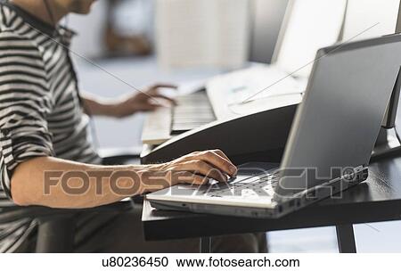 Stock Image - Man using laptop and synth to make music. Fotosearch