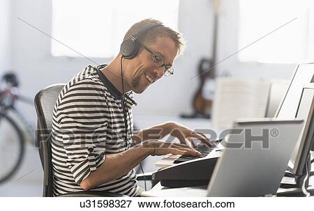 Stock Photo - Man using laptop and synth to make music. Fotosearch