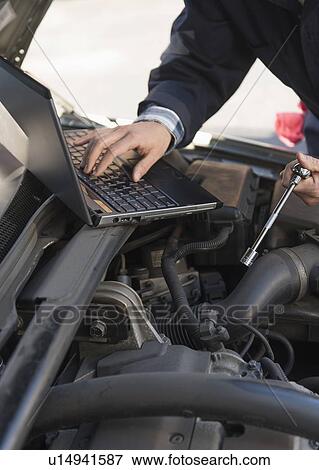 Stock Photo - Mechanic using laptop while repairing car. Fotosearch