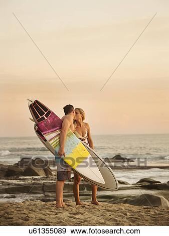 Stock Photo - Mid-adult couple kissing on beach at sunset. Fotosearch