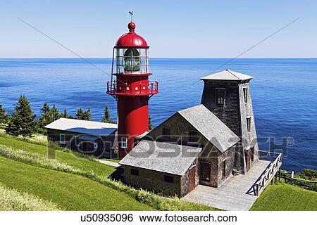 Stock Photograph - Pointe-a-la-Renommee lighthouse and houses against sea at sunny day. Fotosearch