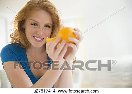 Picture - Portrait of attractive woman peeling orange. Fotosearch