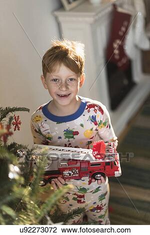 Stock Image - Portrait of boy (6-7) holding toy firetruck. Fotosearch