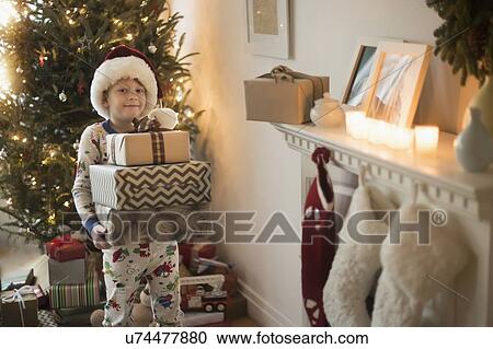 Stock Image - Portrait of boy (6-7) wearing santa claus hat and carrying presents. Fotosearch