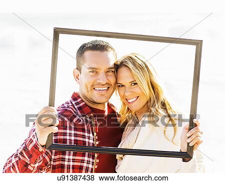 Stock Photo - Portrait of couple holding frame. Fotosearch