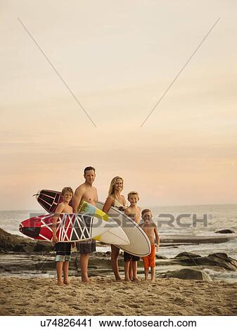 Stock Image - Portrait of family with three children (6-7, 10-11, 14-15) with surfboards on beach. Fotosearch