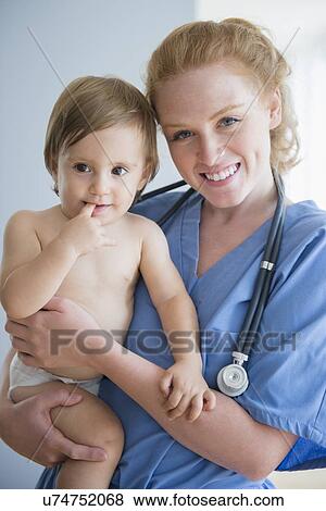 Portrait of female nurse carrying baby boy (12-17 months) View Large Photo Image Stock Photo - Portrait of female nurse carrying baby boy (12-17 months). Fotosearch
