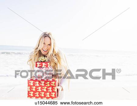 Stock Photography - Portrait of smiling woman holding presents on beach. Fotosearch