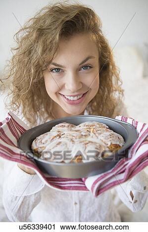 Stock Image - Portrait of smiling young woman holding fresh cinnamon rolls. Fotosearch