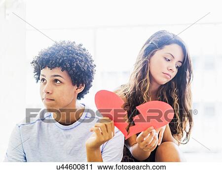 Stock Image - Portrait of young couple with broken heart made from paper. Fotosearch