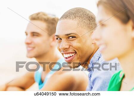Stock Image - Portrait of young man smiling in between defocused friends. Fotosearch