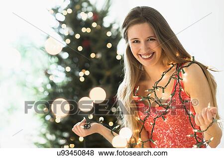 Stock Photo - Portrait of young woman decorating christmas tree with christmas lights. Fotosearch