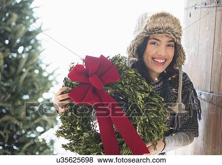 Stock Photo - Portrait of young woman holding Christmas wreath. Fotosearch
