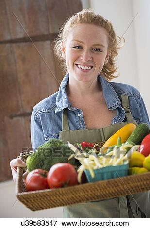Stock Photo - Portrait of young woman holding tray with vegetables. Fotosearch