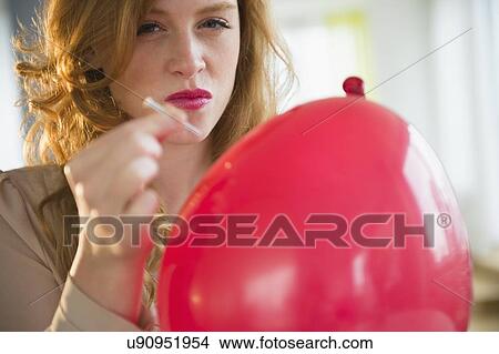 Picture - Portrait of young woman popping balloon. Fotosearch