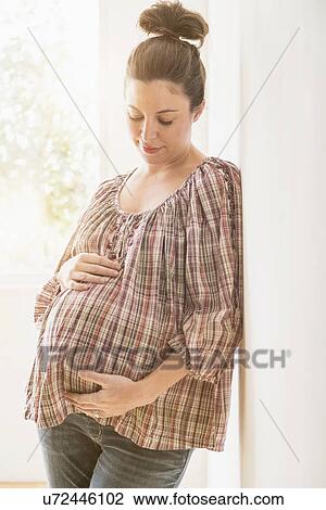 Stock Image - Pregnant woman leaning against wall. Fotosearch