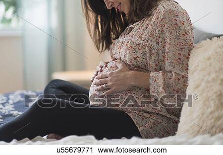 Stock Image - Pregnant woman sitting on bed. Fotosearch