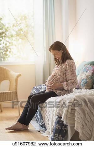 Pregnant woman sitting on bed View Large Photo Image Stock Image - Pregnant woman sitting on bed. Fotosearch