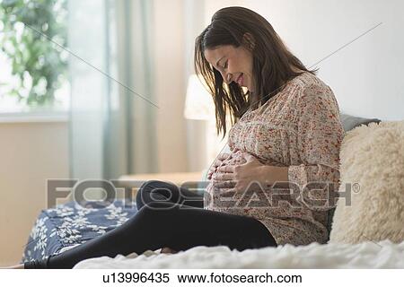 Stock Photography - Pregnant woman sitting on bed. Fotosearch