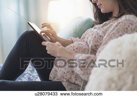 Pregnant woman sitting on bed using tablet View Large Photo Image Stock Image - Pregnant woman sitting on bed using tablet. Fotosearch