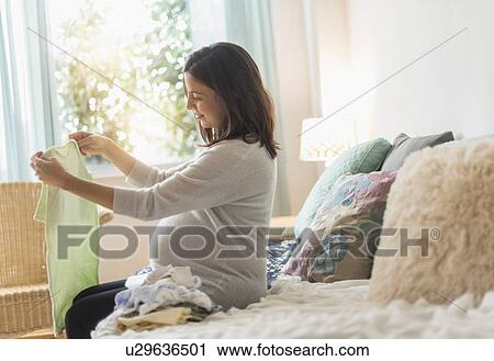 Pregnant woman sitting on bed watching baby clothing View Large Photo Image Stock Image - Pregnant woman sitting on bed watching baby clothing. Fotosearch