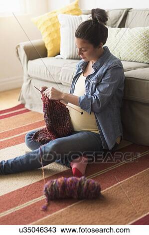 Stock Image - Pregnant woman sitting on floor knitting. Fotosearch