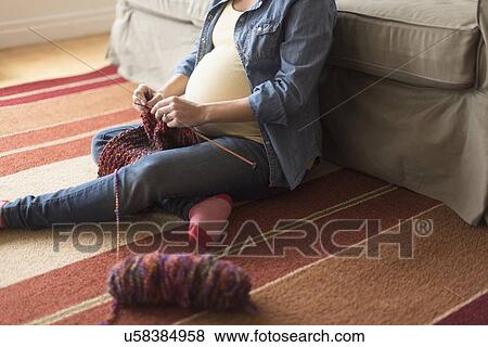 Stock Photo - Pregnant woman sitting on floor knitting. Fotosearch