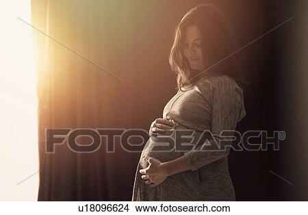 Pregnant woman touching belly at home View Large Photo Image Picture - Pregnant woman touching belly at home. Fotosearch
