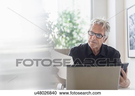 Stock Image - Senior man sitting in home office and using laptop. Fotosearch
