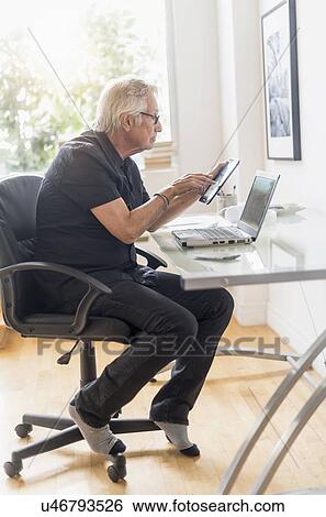 Senior man sitting in home office, using tablet pc View Large Photo Image Stock Photograph - Senior man sitting in home office, using tablet pc. Fotosearch