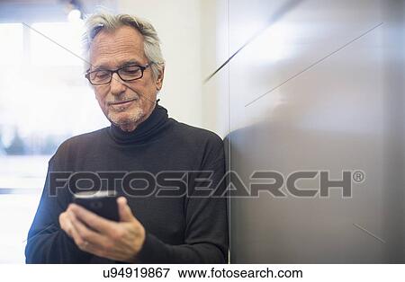 Senior man standing in office corridor and text messaging View Large Photo Image Stock Photo - Senior man standing in office corridor and text messaging. Fotosearch