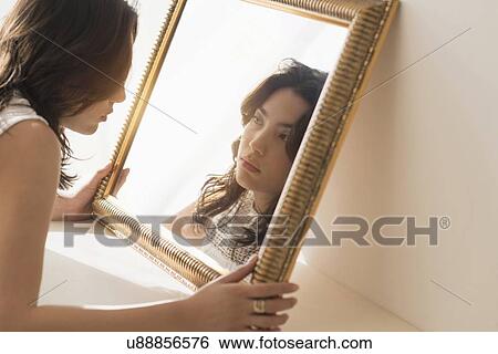 Stock Photograph - Serious young woman looking into mirror. Fotosearch