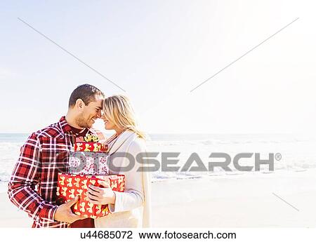 Stock Image - Smiling couple holding presents on beach. Fotosearch