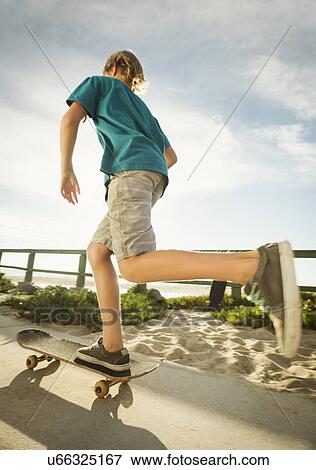 Stock Photo - Teenage boy (14-15) skateboarding on path on beach. Fotosearch