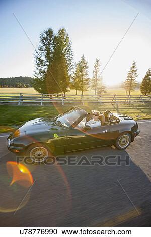 Stock Image - Woman driving convertible car with dog on back seat. Fotosearch
