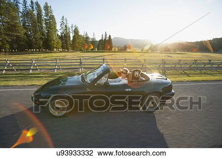 Stock Image - Woman driving convertible car with dog on back seat. Fotosearch