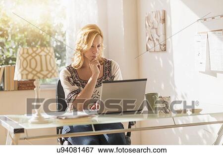 Woman sitting at desk using laptop View Large Photo Image Stock Photo - Woman sitting at desk using laptop. Fotosearch