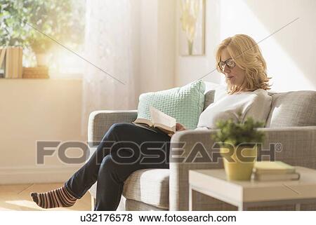 Stock Photo - Woman sitting on sofa and reading book. Fotosearch