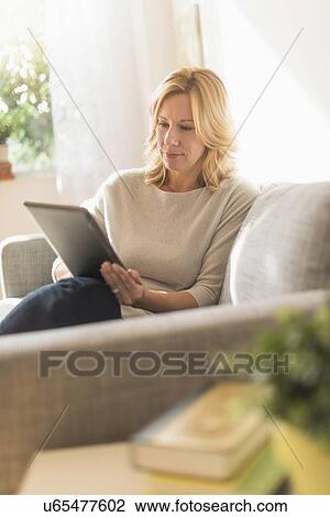 Woman sitting on sofa and using tablet pc View Large Photo Image Stock Image - Woman sitting on sofa and using tablet pc. Fotosearch